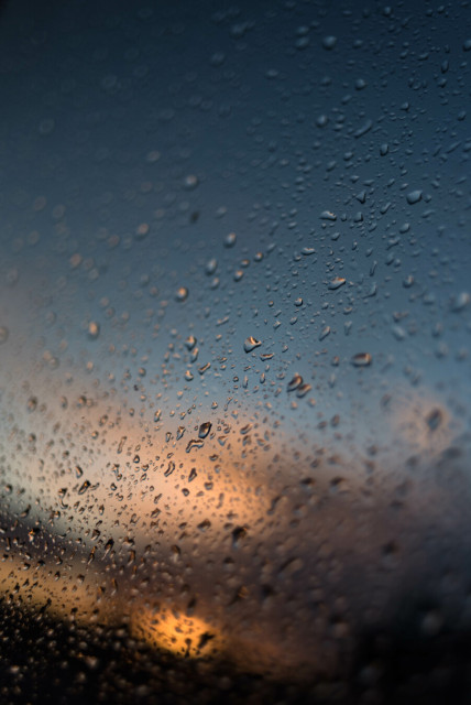 Water drops on glass, sky glows over dark smudges, the rain passed quickly