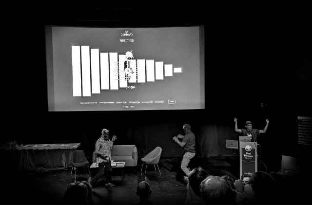 On stage at Pixel Pioneers in Bristol. I'm waving my arms while Bruce and Dave dance in front of the screen wearing owl masks.