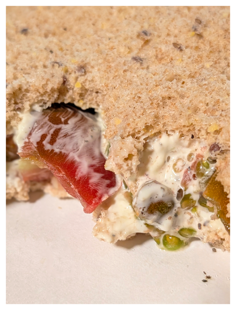 close-up of a tomato sandwich with a couple bites taken out on a white paper plate.