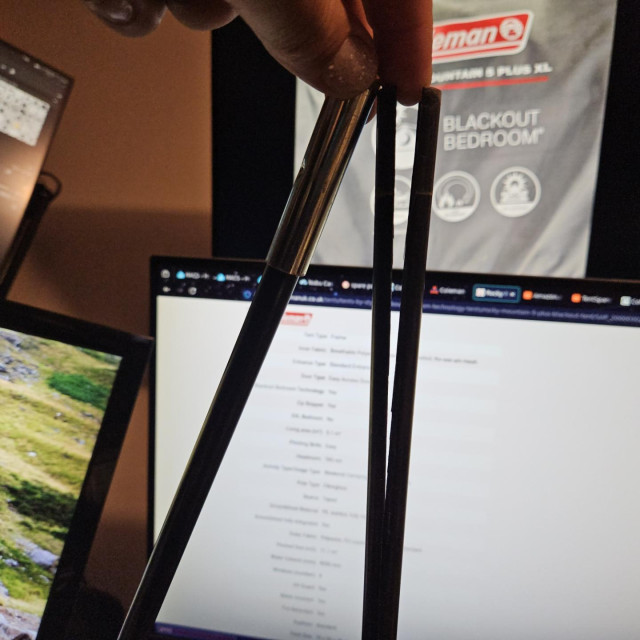 Photo of a sectional tentpole, a finger holes open a longitudinal split from the end of one section. Computer monitors in the background.