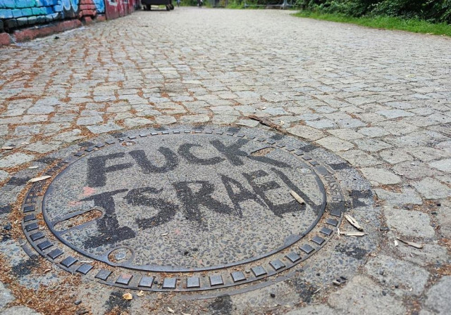 Image of a sewer lid on a street, withe the words "Fuck Israel" written on it.