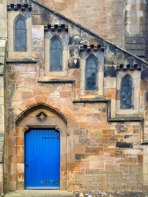 The wall of a church with an arched doorway at ira base, and above this fourn narrow windows are arranged in steps in line with an internal staircase.