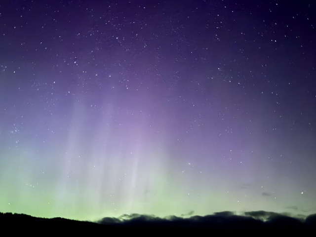 A night sky filled with twinkling stars and soft auroras in shades of purple and green above a dark landscape.