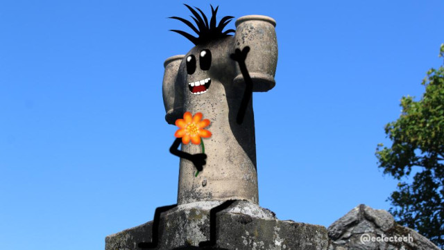 Photo of a grey H shaped chimney against a blue sky. It is angled slightly to the left. I have scribbled on it, addin a smiling face, spiky hair, legs dangling down and arm (one holding a flower, one raised in a wave).