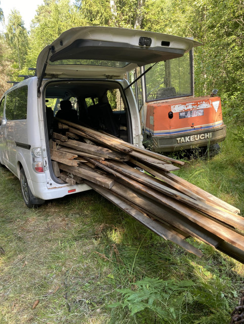 Varebil med åpen bakluke og mange planker stikkende ut