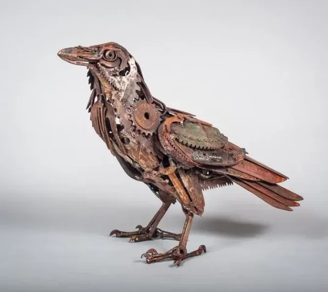 A crow, constructed from welded found objects, specifically rusty old tools and agricultural scrap metal.