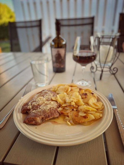 Entrecote provencale with a glass of red wine. The bottle can be seen in the background. A robed skeleton (death?) is on the bottle label.