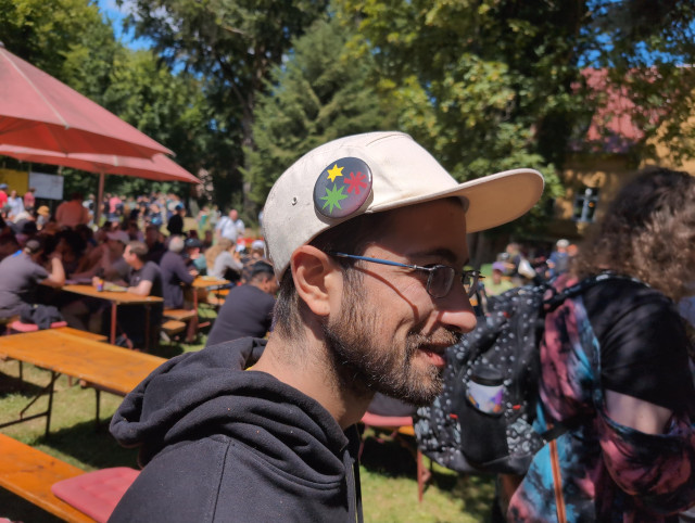 A human with a hat with a botton on it with a multi colored asterism 