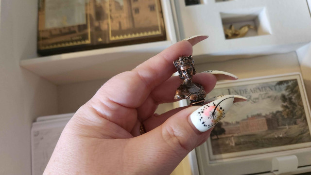 Holding one of the player pieces, a small bronze bust of a person with their hair in a beautiful regency updo.