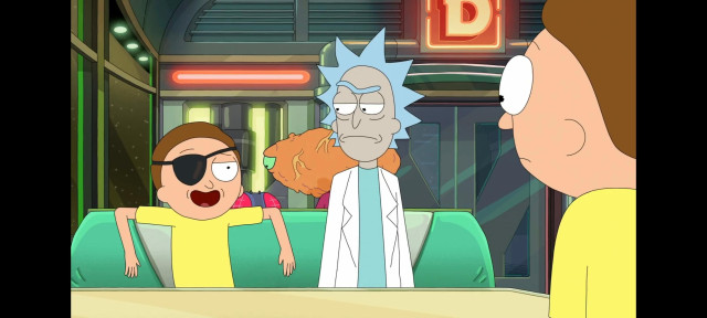 A screenshot from season 9 of Rick and Morty. Evil Morty sits next to Rick at a space diner looking smug. Rick is not impressed and regular Morty looks on with concern.