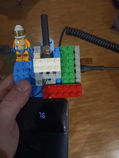 Photo with LEGO built fixture for Heltec V3 Meshcore companinion with stock antenna inside a rubber tire. Also power bank, a LEGO figurine and a few wires visible.