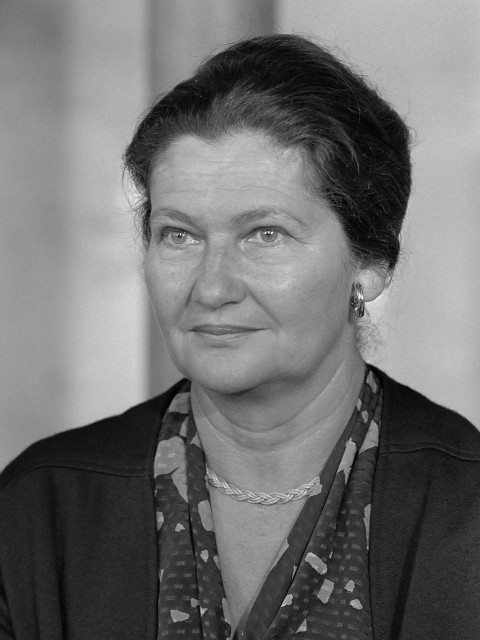 Image en noir et blanc de Simone Veil, vêtue d’une veste noire et d’un chemisier à motif de taches. Elle porte un collier en chaîne et des boucles d’oreilles.
