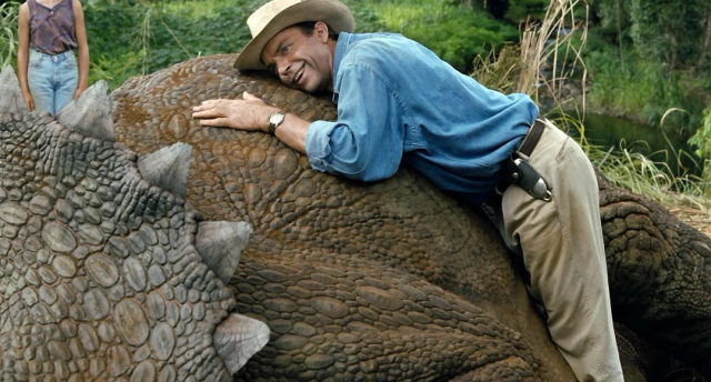 This is a photographic still from the movie, Jurassic Park. Sam dressed up as his character is listening to a breathing triceratops.