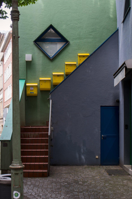 Treppenaufgang mit gelben Briefkästen an einer grünen Wand und blauem Türbereich in einem Innenhof