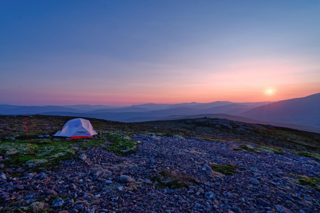 An image of a tent on a mountain top with a sunset in the distance.