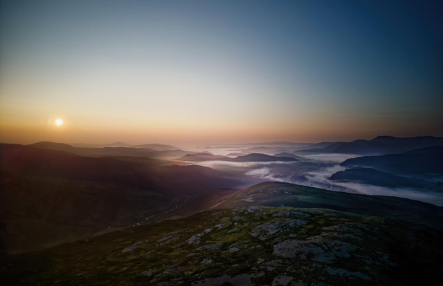 An image of a sunrise from a mountain top looking down on a cloudy river valley.