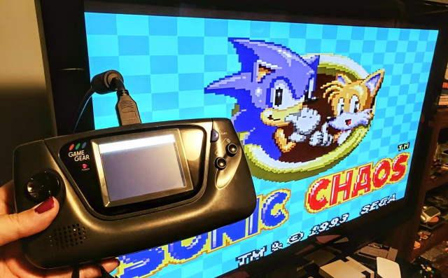 My Game Gear in the foreground with an HDMI cable connected and the TV screen behind it displaying the Game Gear game