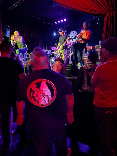 Fang performing a song. A skinhead is watching in front of the stage with a t-shirt showing a klan member with a “no” symbol over it.