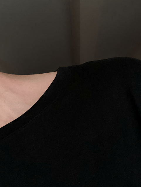 Low light photo of the photographer, wearing a dark t-shirt, leaning out of the frame and exposing part of their bare neck and shoulder.