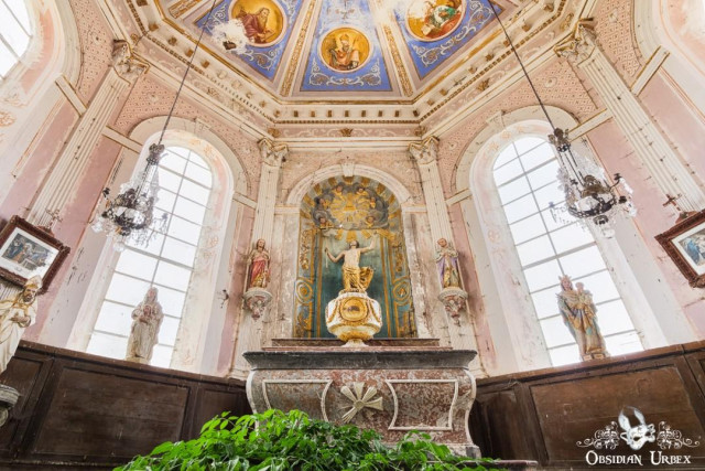 An ornate, decaying chapel interior features a detailed painted ceiling, religious statues, and a central altar. A small tree grows in the foreground.
