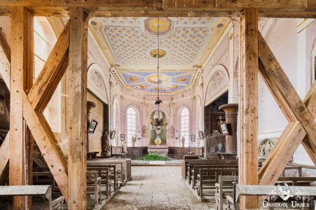 Chapel interior framed by wooden beams, showcasing elaborate painted ceilings and dusty pews.