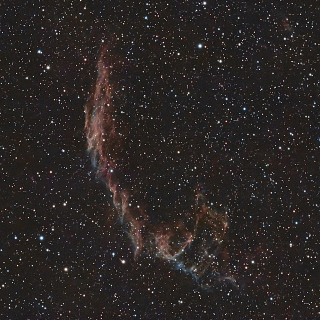Image of a nebula set against the backdrop of numerous stars, showcasing intricate patterns and colors in shades of red and blue.