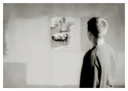 20s man with short hair, wearing a dark cardigan faces a movie poster. other bills have been painted over.