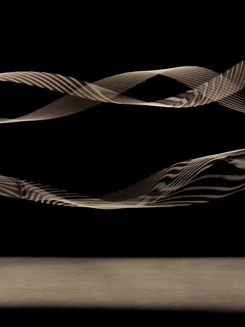 A photo of a dark room with two pairs of  long elastic strings rotating quickly under spotlights. A striped pattern of shadows appears on the motion blurring strings. 