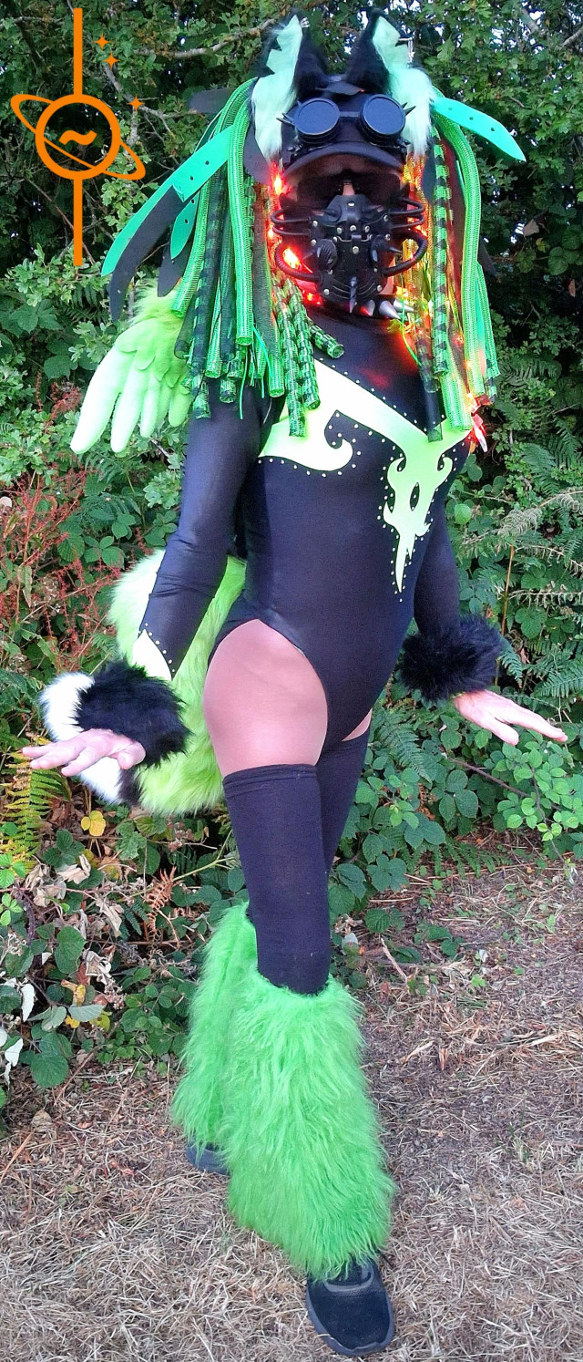 Cybergoth fox in green, stood in front of a Bush.