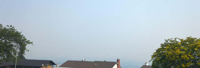 A view that should be of a river valley is nearly completely obscured by grey smoke, with a couple of house rooves and treetops in the bottom foreground.