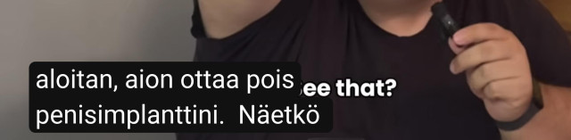 Osittainen kuvakaappaus YouTube videosta. Automaattinen käännöstekstitys suomen kielellä mustalla taustalla, jossa lukee ”aloitan, aion ottaa pois penisimplanttini. Näetkö”