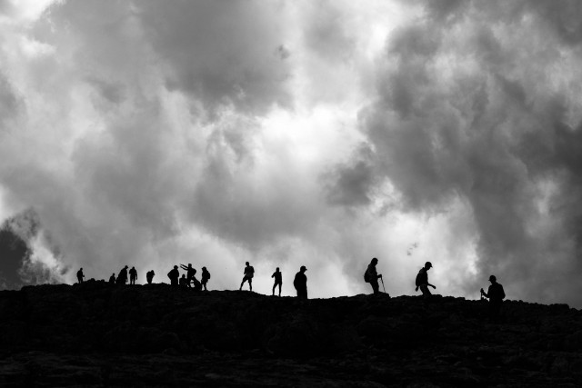Ein Bergkamm auf dem sich viele Menschen tummeln. Es ist ein schwarzweißes Foto und die Menschen sind nur als Silhouetten erkennbar.