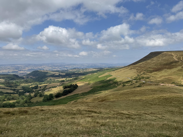 View from a mountain across across miles and miles of Mid Wales countryside. Green and golden fields, hedges and woods as far as the eye can see. 