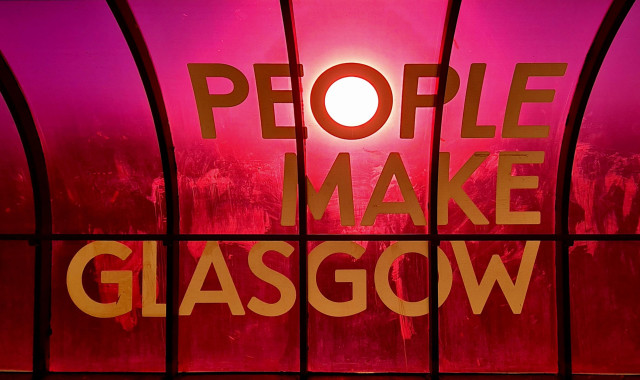 A sign which reads People Make Glasgow, with the evening sun lined with the O in People, creating a halo around it.