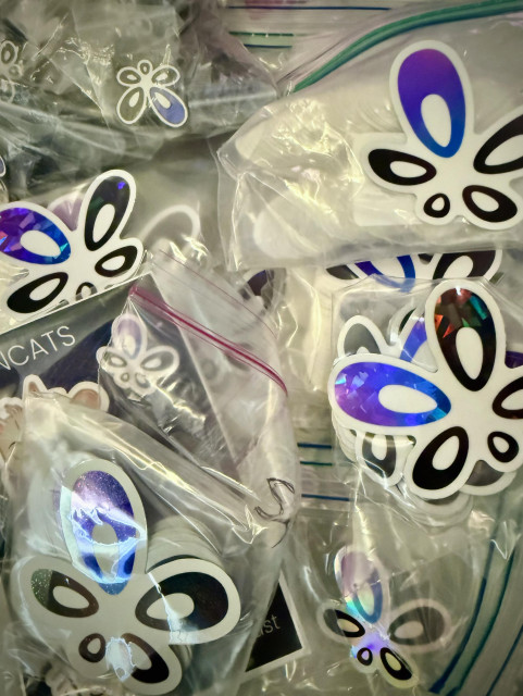 A pile of Owncast logo stickers and pins of different styles and sizes. 