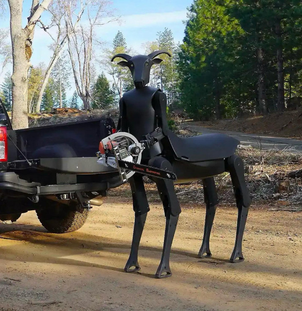 A matte-black robot shaped like a four-legged goat or centaur with curved horns standing on a dirt road outdoors. The robot holds a chainsaw equipped with a circular handguard in its right mechanical arm. To its left is the open tailgate of a dark pickup truck, with a forest and clear sky visible in the background.