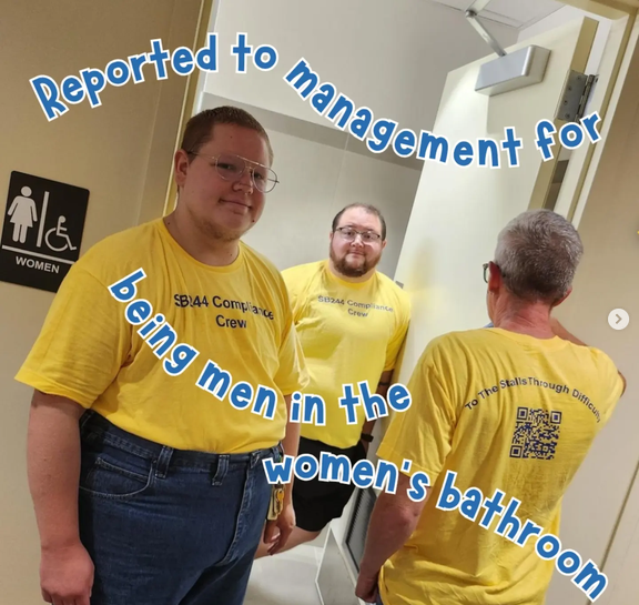 Three trans men are standing around the open door of a women's bathroom in yellow shirts that say "SB244 Compliance Crew." Text reads "Reported to management for being men in the women's bathroom."