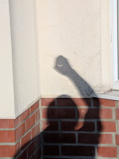 My shadow against a wall, with the hand against beige render making a pinhole to project the sun and the head and shoulders lower against brick