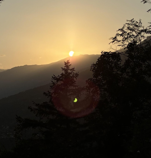 Sun barely above mountain, slightly eclipsed. Green reverted phantom image of same sun below.