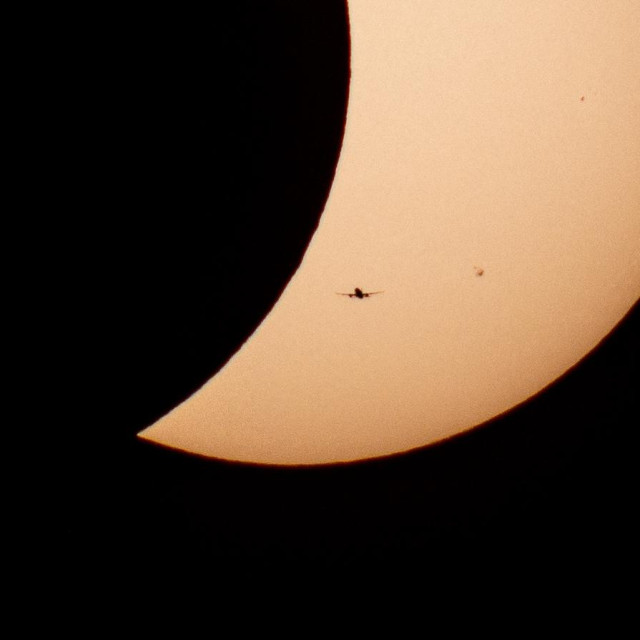 Photo of Solar Eclipse with a crescent sun and a plane silhouette.