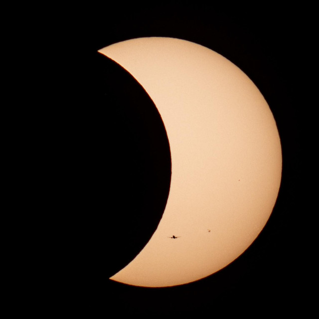 Photo of Solar Eclipse with a crescent sun and a plane silhouette.