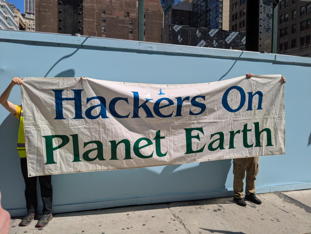 An old Hackers on Planet Earth banner held up in front of the Hotel Pennsylvania site.