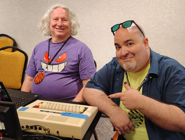 The Undersigned posing with a very nice man known as Henry "Strick" Strickland, and his TRS-80 Color Computer 2. The Undersigned is pointing admiringly at the CoCo.
