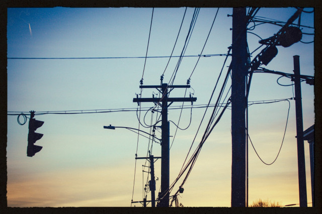 sunset photo of roughly five utility poles, criscrossing power lines and a hanging street crossing light