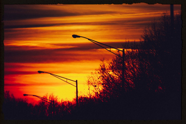 ridiculously vibrant sunset photo of three streetlamps that haven't been illuminated yet, standing in silhouette against a red striped sky 