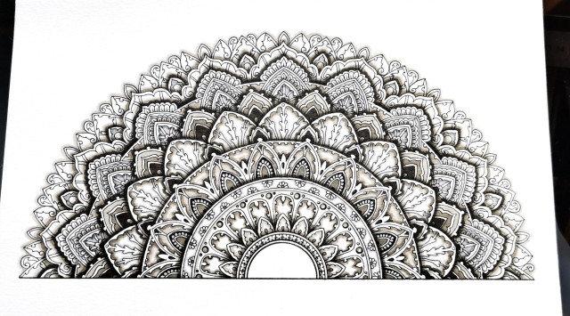 A semi-circle mandala on white paper. It's drawn with black ink, and shaded in warm greys that give it a 3D layered feel. 