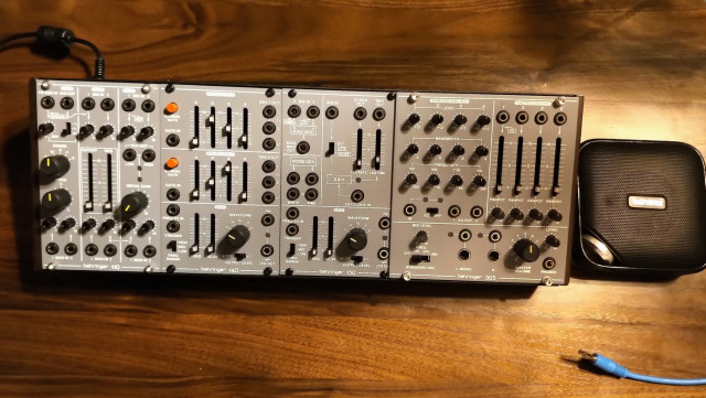 A modular synthesizer skiff and speaker on a table. The modular has all the basic function modules.
