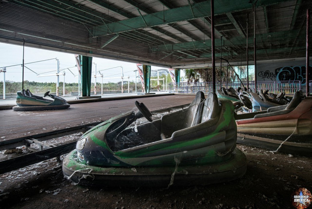 A green, purple, and black bumper car, with other cars in the ride in the background. Beyond the ride boundary trees and lights are visible